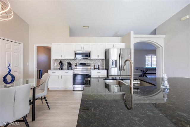 kitchen with white cabinets, stainless steel appliances, tasteful backsplash, and dark stone counters