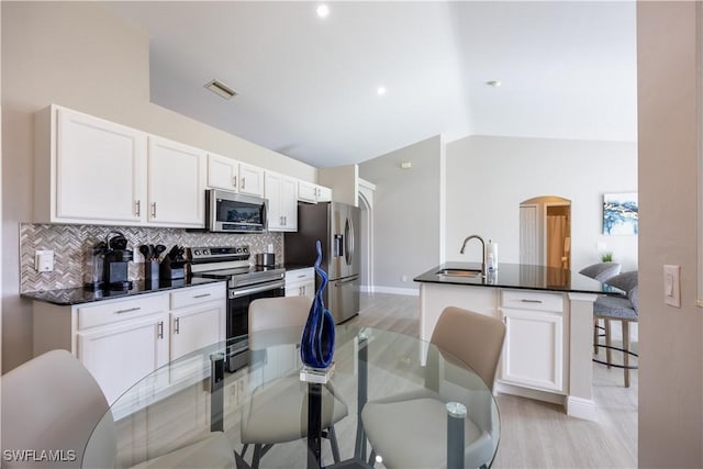 kitchen with white cabinetry, stainless steel appliances, lofted ceiling, decorative backsplash, and a breakfast bar