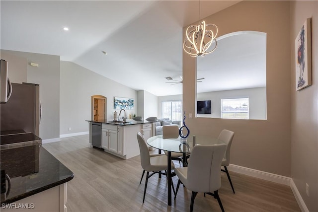 dining area featuring ceiling fan with notable chandelier, light wood-type flooring, sink, and vaulted ceiling