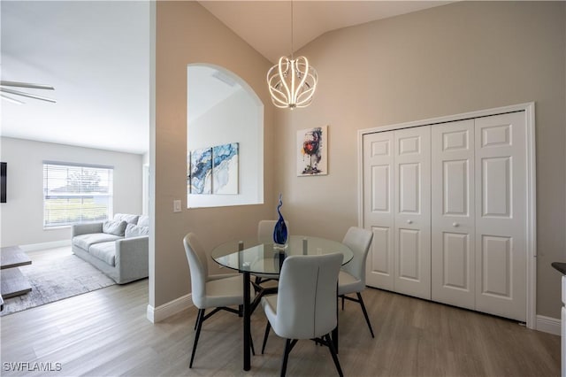 dining space with ceiling fan with notable chandelier, light hardwood / wood-style floors, and lofted ceiling