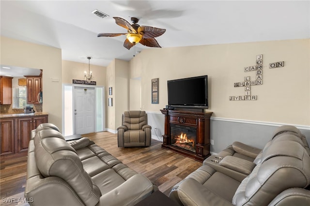 4560 Key Largo Ln, Bonita Springs, FL 34134 - living area with a ceiling fan, wood finished floors, a glass covered fireplace, vaulted ceiling, and a chandelier