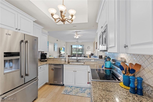 kitchen with stainless steel appliances, sink, ceiling fan with notable chandelier, and white cabinets