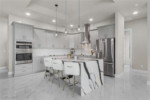 kitchen with a kitchen island with sink, a kitchen breakfast bar, wall chimney exhaust hood, appliances with stainless steel finishes, and decorative light fixtures