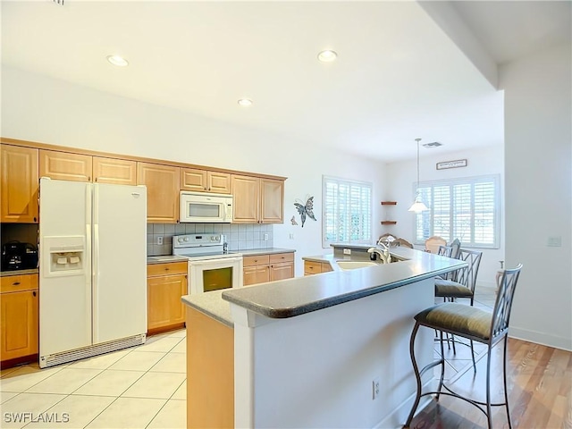 kitchen featuring sink, a center island with sink, a kitchen breakfast bar, white appliances, and decorative backsplash