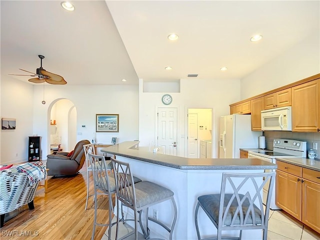 kitchen with white appliances, ceiling fan, a kitchen breakfast bar, a center island, and washer / dryer