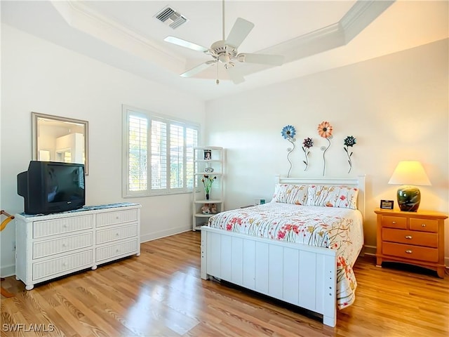 bedroom with crown molding, light hardwood / wood-style flooring, a raised ceiling, and ceiling fan