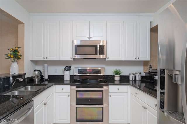 kitchen with appliances with stainless steel finishes, white cabinetry, dark stone countertops, and sink