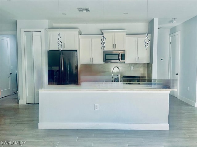 kitchen with hanging light fixtures, tasteful backsplash, black refrigerator with ice dispenser, a kitchen island with sink, and white cabinets