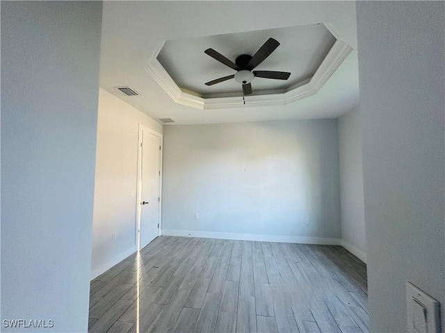 spare room featuring light wood-type flooring, a tray ceiling, and ceiling fan