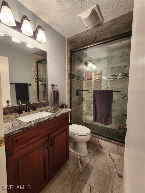 bathroom with vanity, an enclosed shower, a textured ceiling, and toilet