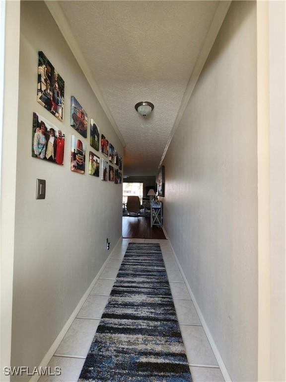 corridor with crown molding, light tile patterned flooring, and a textured ceiling