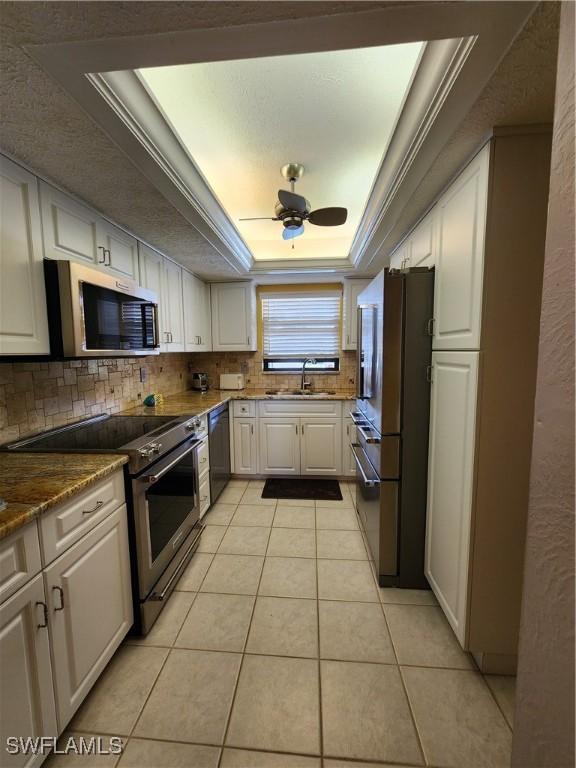 kitchen featuring appliances with stainless steel finishes, ornamental molding, a raised ceiling, white cabinetry, and light tile patterned flooring