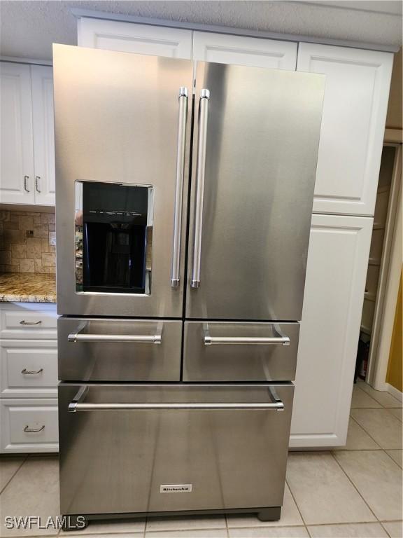 kitchen with light tile patterned floors, high quality fridge, white cabinets, light stone countertops, and backsplash