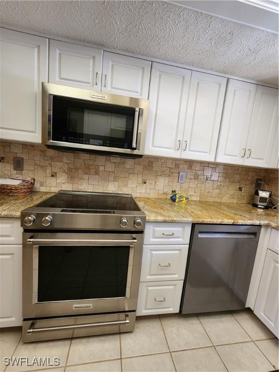 kitchen with light stone countertops, light tile patterned floors, white cabinetry, and appliances with stainless steel finishes