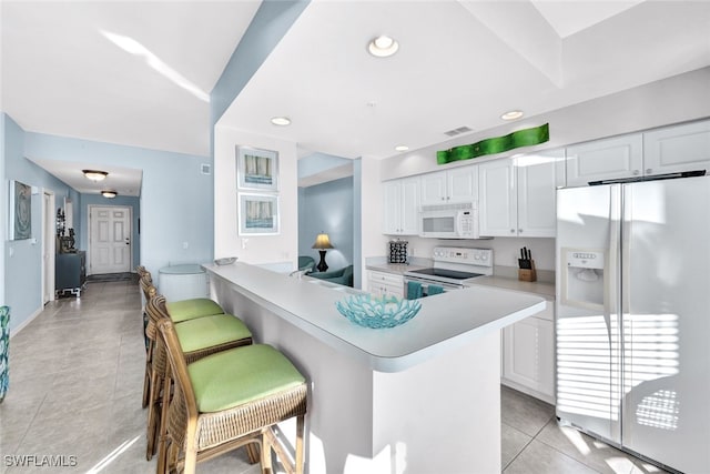 kitchen with white cabinetry, kitchen peninsula, white appliances, a breakfast bar, and light tile patterned floors