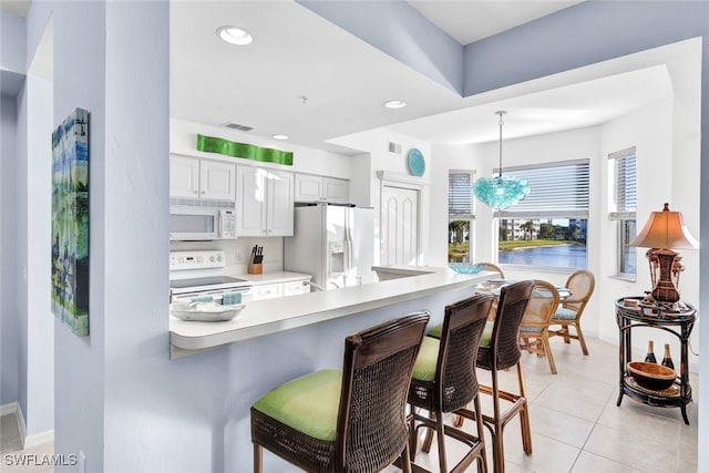 kitchen with white appliances, white cabinets, a kitchen breakfast bar, decorative light fixtures, and light tile patterned flooring