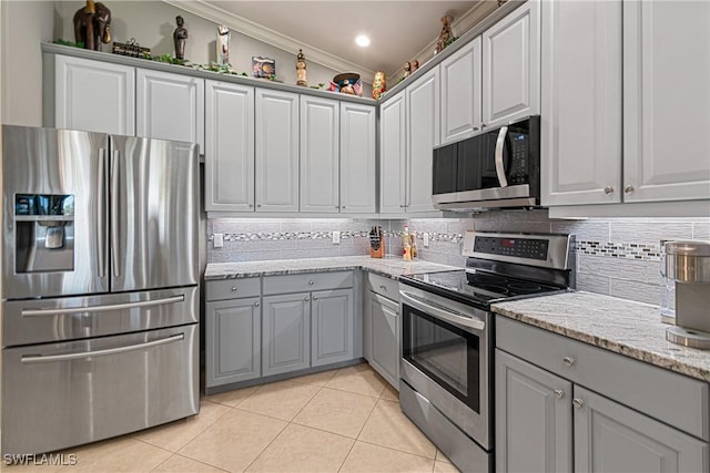 kitchen with gray cabinetry, light stone countertops, ornamental molding, light tile patterned floors, and stainless steel appliances