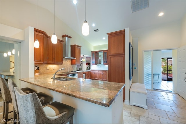 kitchen featuring kitchen peninsula, wall chimney exhaust hood, vaulted ceiling, sink, and pendant lighting