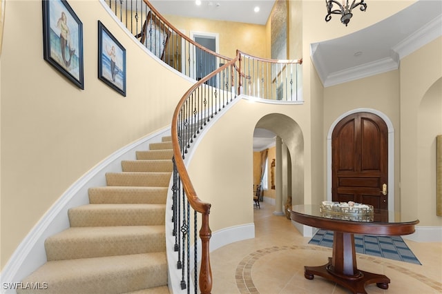 entryway featuring a chandelier, a high ceiling, crown molding, and light tile patterned flooring