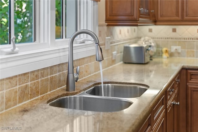 kitchen with backsplash, light stone counters, and sink