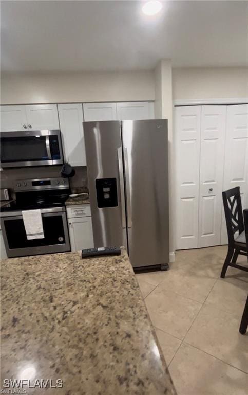 kitchen with white cabinetry, stainless steel appliances, light stone countertops, and light tile patterned floors