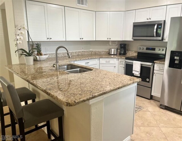 kitchen featuring sink, appliances with stainless steel finishes, a kitchen breakfast bar, white cabinets, and kitchen peninsula