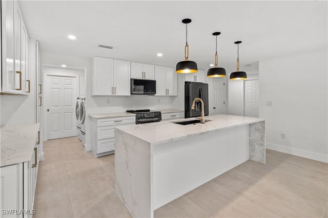 kitchen with white cabinetry, an island with sink, light stone countertops, washing machine and dryer, and black appliances