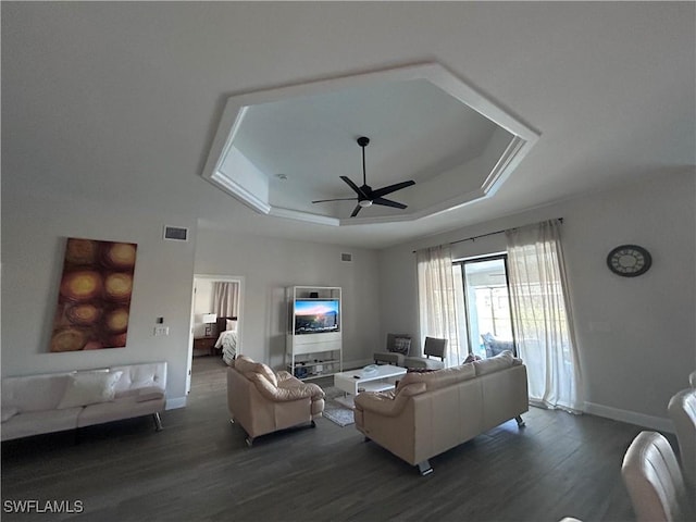 living room featuring ceiling fan, dark hardwood / wood-style flooring, and a tray ceiling