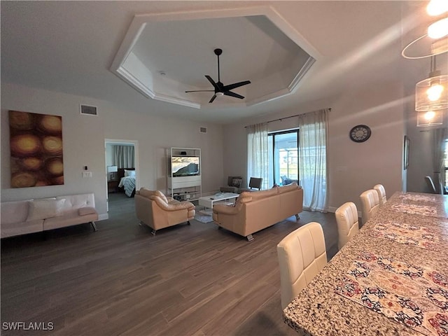 living room featuring a raised ceiling, ceiling fan, and dark wood-type flooring