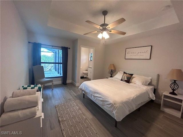 bedroom with a raised ceiling, ensuite bath, ceiling fan, and dark wood-type flooring