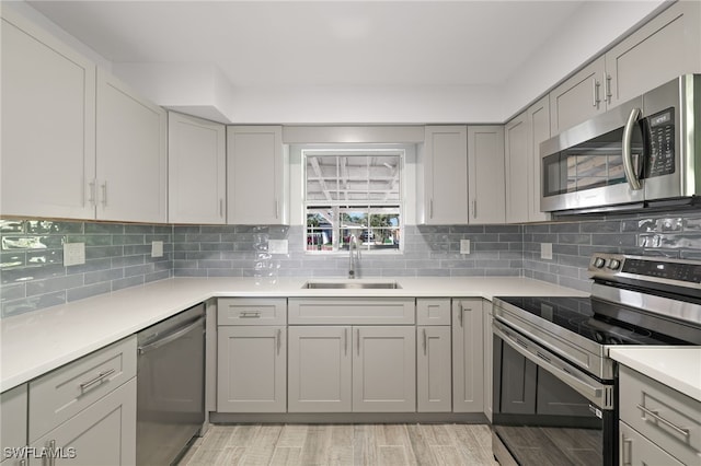 kitchen with gray cabinetry, decorative backsplash, sink, and appliances with stainless steel finishes