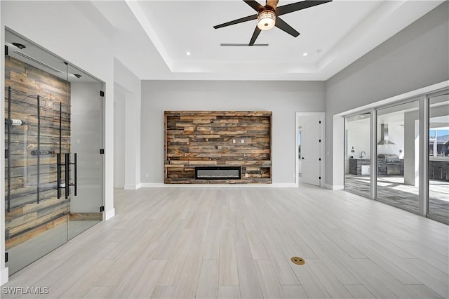 unfurnished living room with ceiling fan, light hardwood / wood-style floors, a raised ceiling, and a fireplace