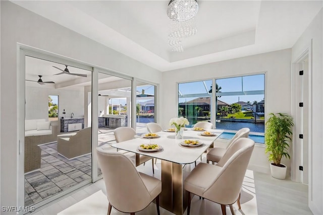 dining room with a tray ceiling, a water view, and ceiling fan with notable chandelier