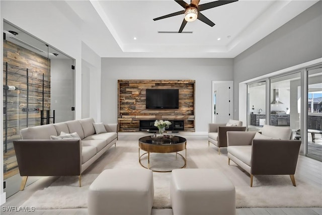 living room featuring a raised ceiling, a stone fireplace, and ceiling fan