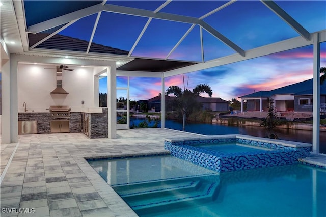 pool at dusk with an in ground hot tub, an outdoor kitchen, glass enclosure, and a grill