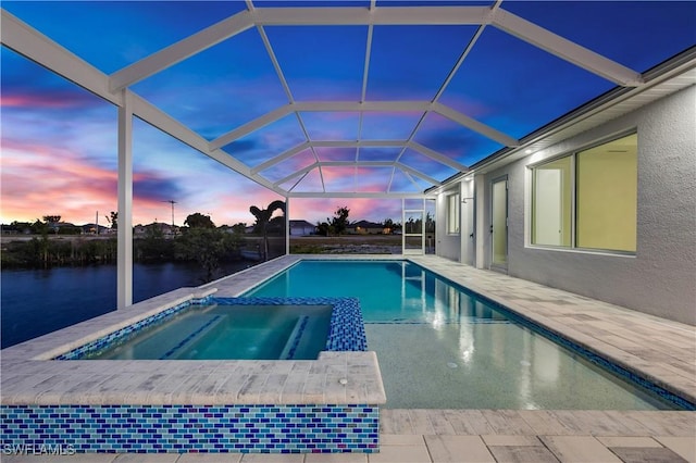 pool at dusk featuring a lanai, a patio area, an in ground hot tub, and a water view