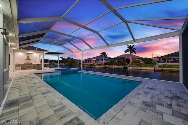 pool at dusk featuring a lanai, a patio area, a water view, and an outdoor kitchen