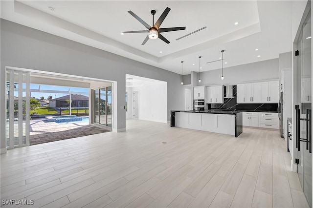 kitchen with a towering ceiling, a raised ceiling, ceiling fan, decorative light fixtures, and white cabinetry