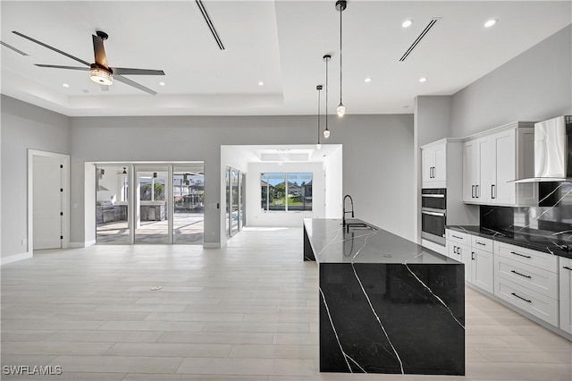 kitchen with wall chimney exhaust hood, a raised ceiling, sink, hanging light fixtures, and a large island