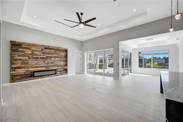 unfurnished living room with a raised ceiling, ceiling fan, and light wood-type flooring