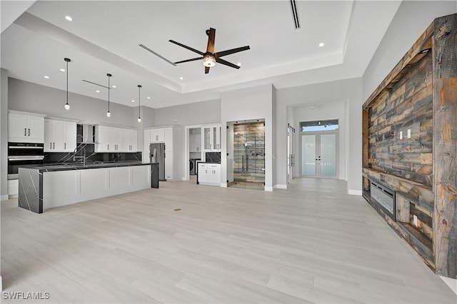 unfurnished living room featuring a raised ceiling, ceiling fan, french doors, and a towering ceiling