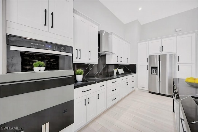 kitchen with decorative backsplash, stainless steel fridge, wall chimney range hood, dark stone countertops, and white cabinets