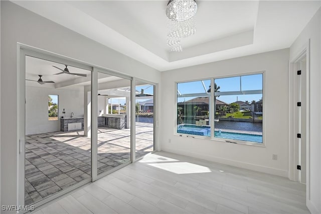 spare room with ceiling fan with notable chandelier, a water view, light hardwood / wood-style flooring, and a tray ceiling