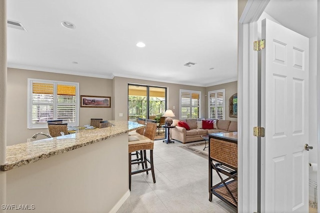 kitchen featuring light stone countertops, light tile patterned flooring, a breakfast bar area, and ornamental molding