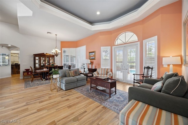 living room featuring a raised ceiling, french doors, a chandelier, and light hardwood / wood-style flooring