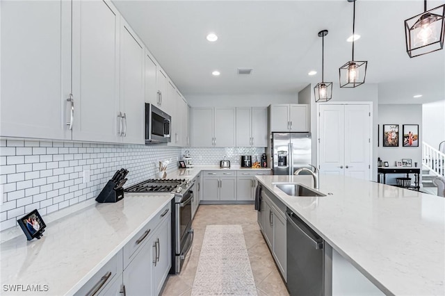 kitchen with light stone countertops, sink, stainless steel appliances, pendant lighting, and decorative backsplash