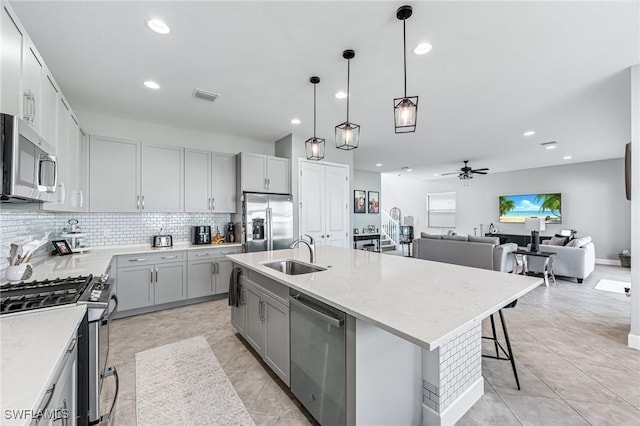 kitchen featuring ceiling fan, sink, stainless steel appliances, an island with sink, and pendant lighting