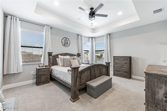 bedroom featuring ceiling fan, a raised ceiling, light colored carpet, and multiple windows