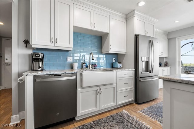 kitchen with sink, light hardwood / wood-style flooring, stainless steel appliances, light stone countertops, and white cabinets