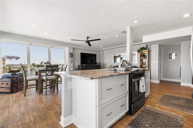 kitchen featuring black electric range oven, a center island with sink, white cabinets, and ceiling fan